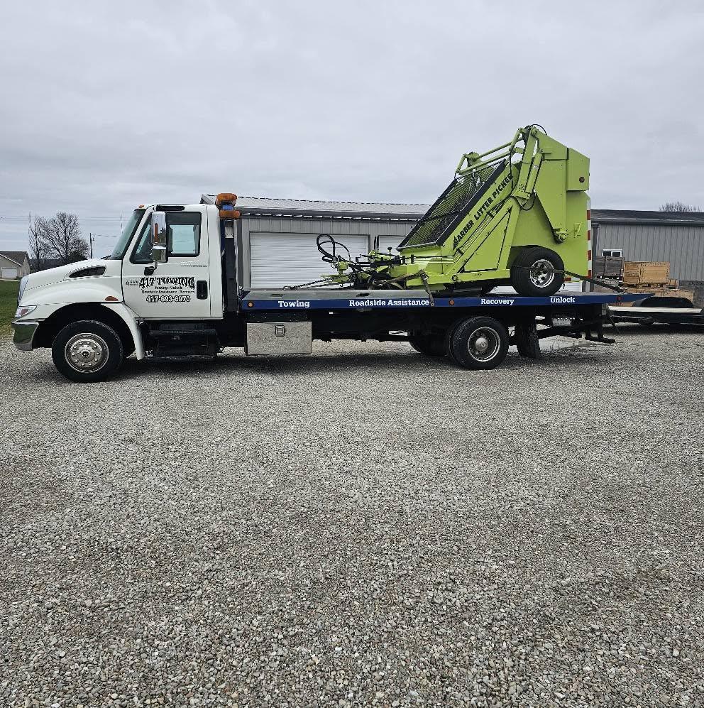 A 417 Towing flatbed carrying a green industrial litter picker machine